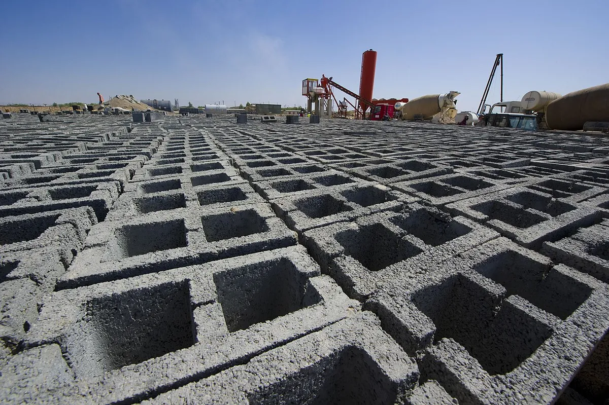 Rows of new hollow concrete blocks curing in a block yard, their open cells facing up